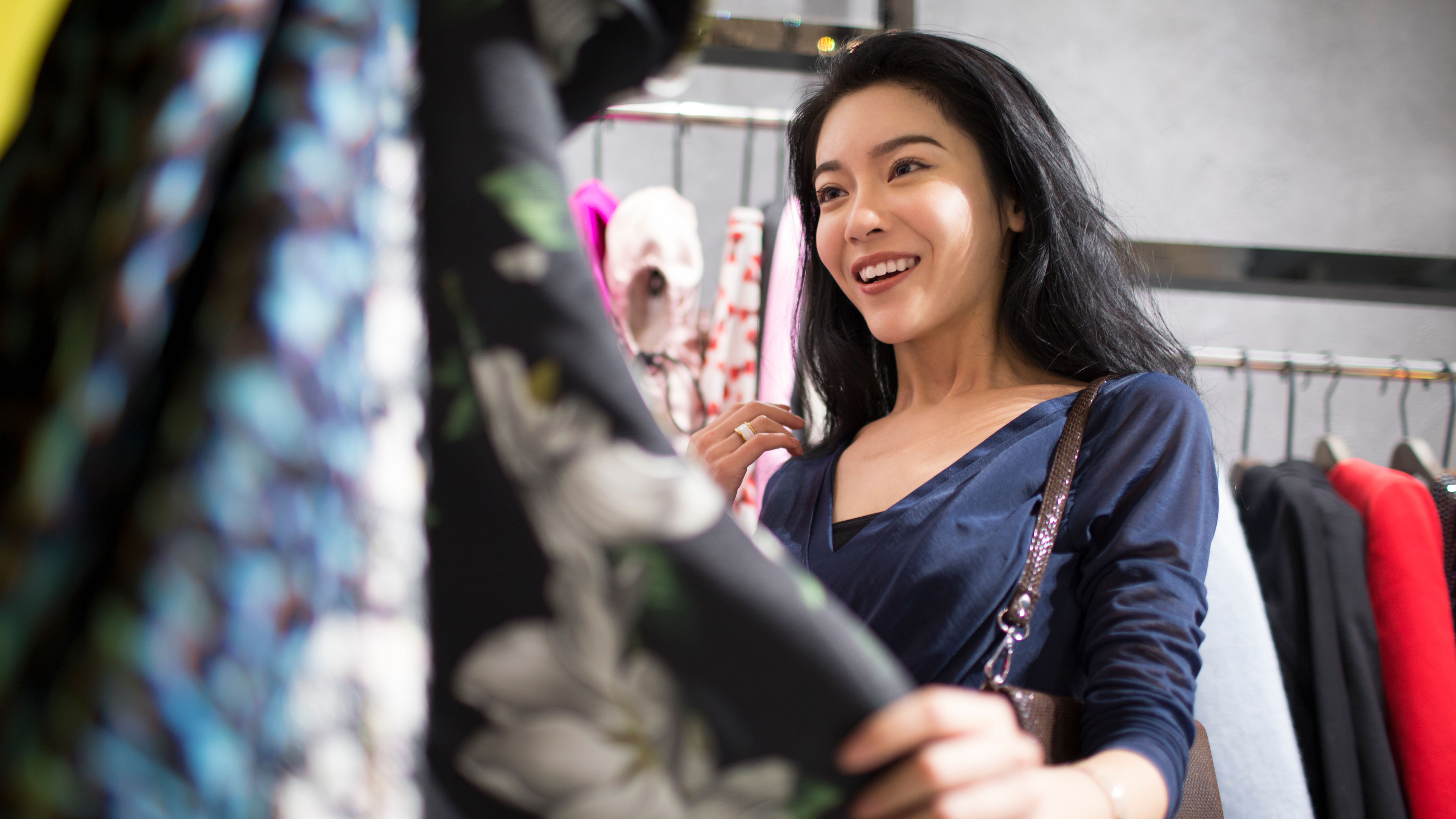 A smiling woman shopping for clothes, excitedly browsing through dresses in a fashion store.